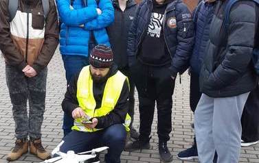 Nauczyciel demonstruje działanie drona. Sześciu uczni&oacute;w przygląda się mu.
