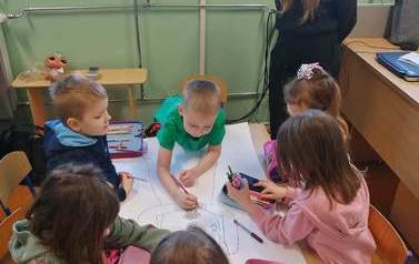 Uśmiechnięta uczennica klasy si&oacute;dmej przygląda się pracy kilkorga dzieci z zer&oacute;wki.