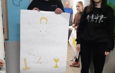 Uczeń i uczennica klasy &oacute;smej prezentują plakat na temat sakramentu bierzmowania.