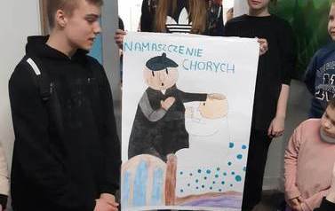 Uczniowie i uczennice klasy si&oacute;dmej prezentują plakat na temat namaszczenia chorych.