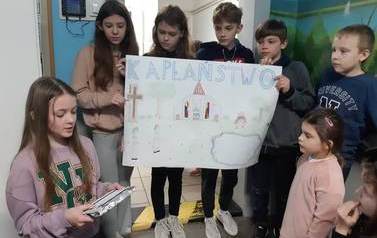 Uczennice i uczniowie klasy piątej prezentują plakat na temat kapłaństwa.