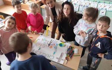 Uczniowie i uczennice klasy pierwszej i drugiej wraz z wychowawczynią wykonują plakat na temat chrztu.