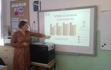 Wicedyrektor szkoły prezentuje slajd z wynikami egzamin&oacute;w zawodowych uczni&oacute;w ekonomiaka.