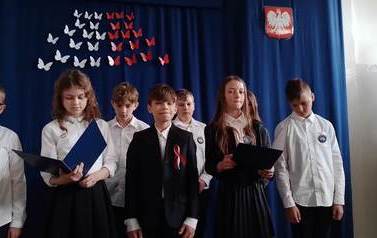 Elegancko ubrani chłopcy i dziewczęta na tle biało-czerwonej dekoracji.