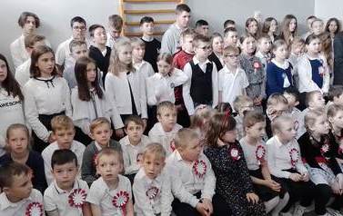 Na galowo ubrani uczniowie, przystrojeni w biało-czerwone kotyliony zgromadzili się w szkolnej sali, aby obejrzeć przedstawienie.