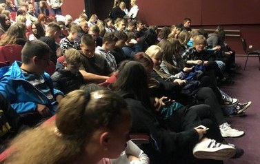 Kolorowo ubrani uczniowie zajmują miejsca na widowni.