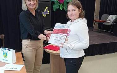 Uczennica prezentuje dyplom, kt&oacute;ry wręcza jej stojąca obok kobieta.