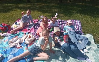 Uśmiechnięte dzieci siedzą w parku na kocyku.