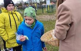 Na zdjęciu nauczycielka częstuje słodyczami stojące w rzędzie dzieci: chłopca i dwie dziewczynki.