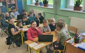 Uczniowie podzieleni na grupy siedzą przy stolikach.