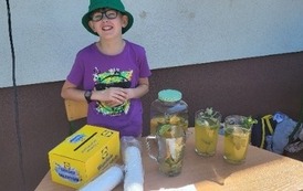 Uczeń w zielonej czapce i fioletowej bluzce sprzedaje lemoniadę.
